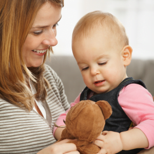 Connection is the foundation of humanity. Mum and toddler cuddle whilst looking at Teddy. Mum smiling lovingly at her daughter