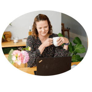 Liz Farrant smiling at the laptop whilst holding a white mug. Conducting a virtual consultation.