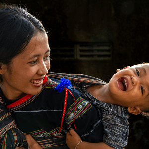 Mum with toddler in sling on her back, both are laughing